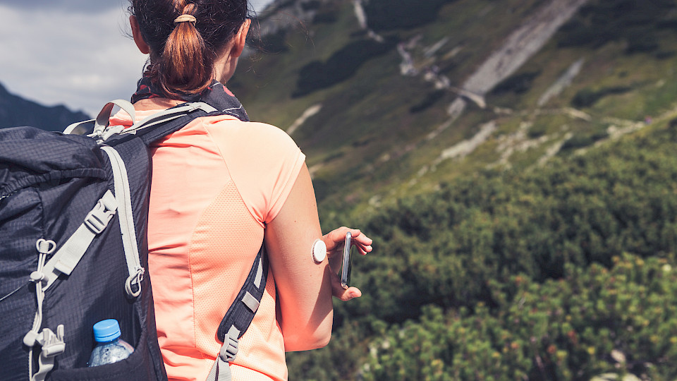 Eine Frau überprüft beim Wandern den Glukosegehalt mit einem Fernsensor und Mobiltelefon. (Bild: Shutterstock.com/Lukasz Pawel Szczepanski)